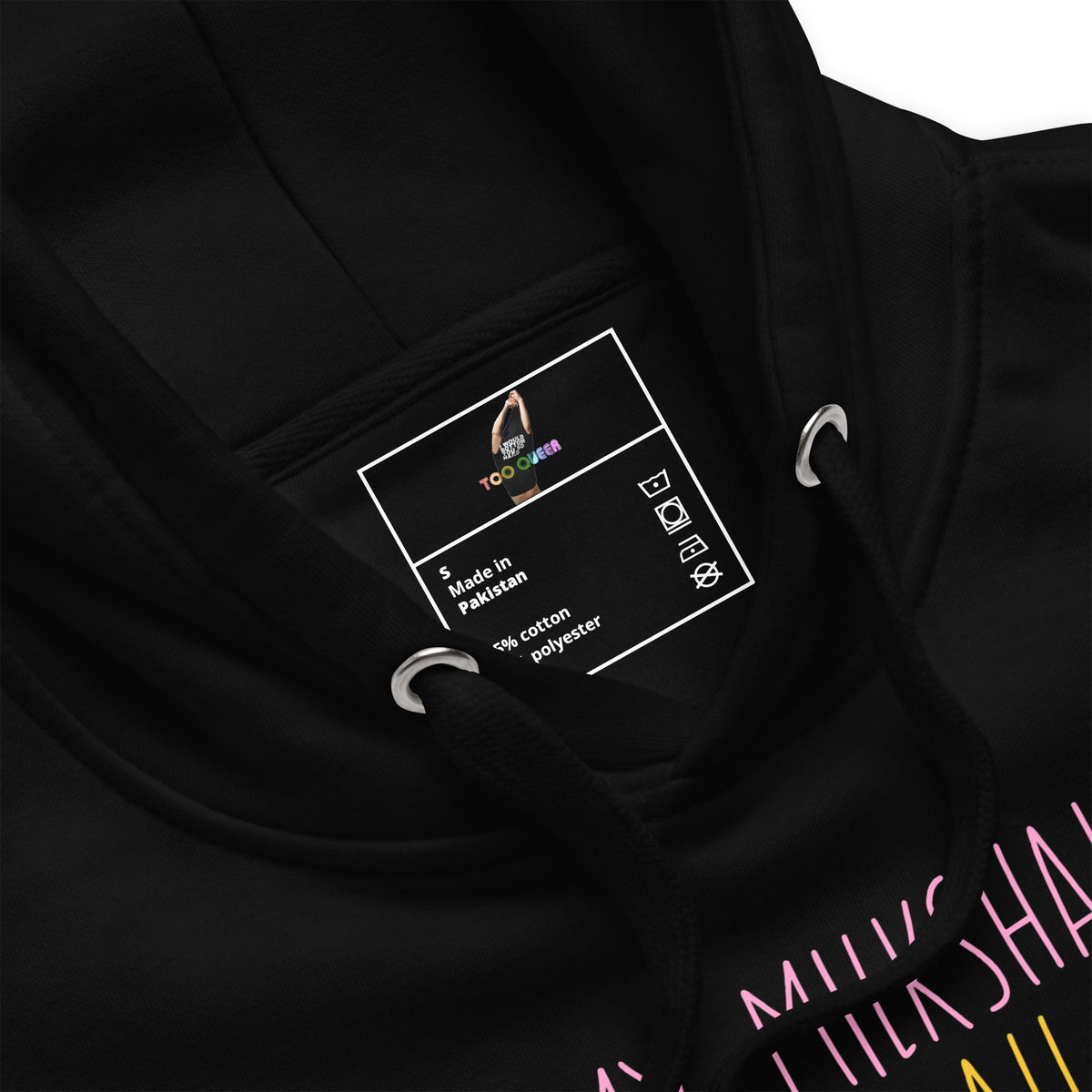 Close-up of a black hoodie interior neck label with a white printed insert card showing the TOO FINE brand, alongside metal drawstring rings and part of a pink and yellow graphic print on the sleeve.