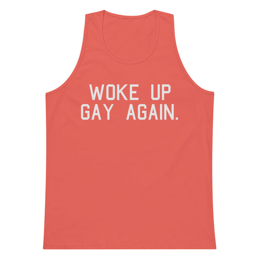 A coral pink tank top with the phrase 'WOKE UP GAY AGAIN.' printed in bold white capital letters across the chest, shown against a plain white background.