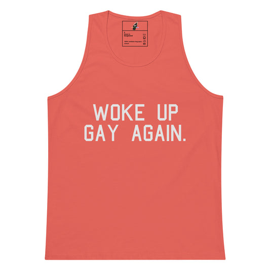 A coral pink sleeveless tank top with the phrase 'WOKE UP GAY AGAIN.' printed in bold white capital letters across the chest, shown flat against a plain white background.