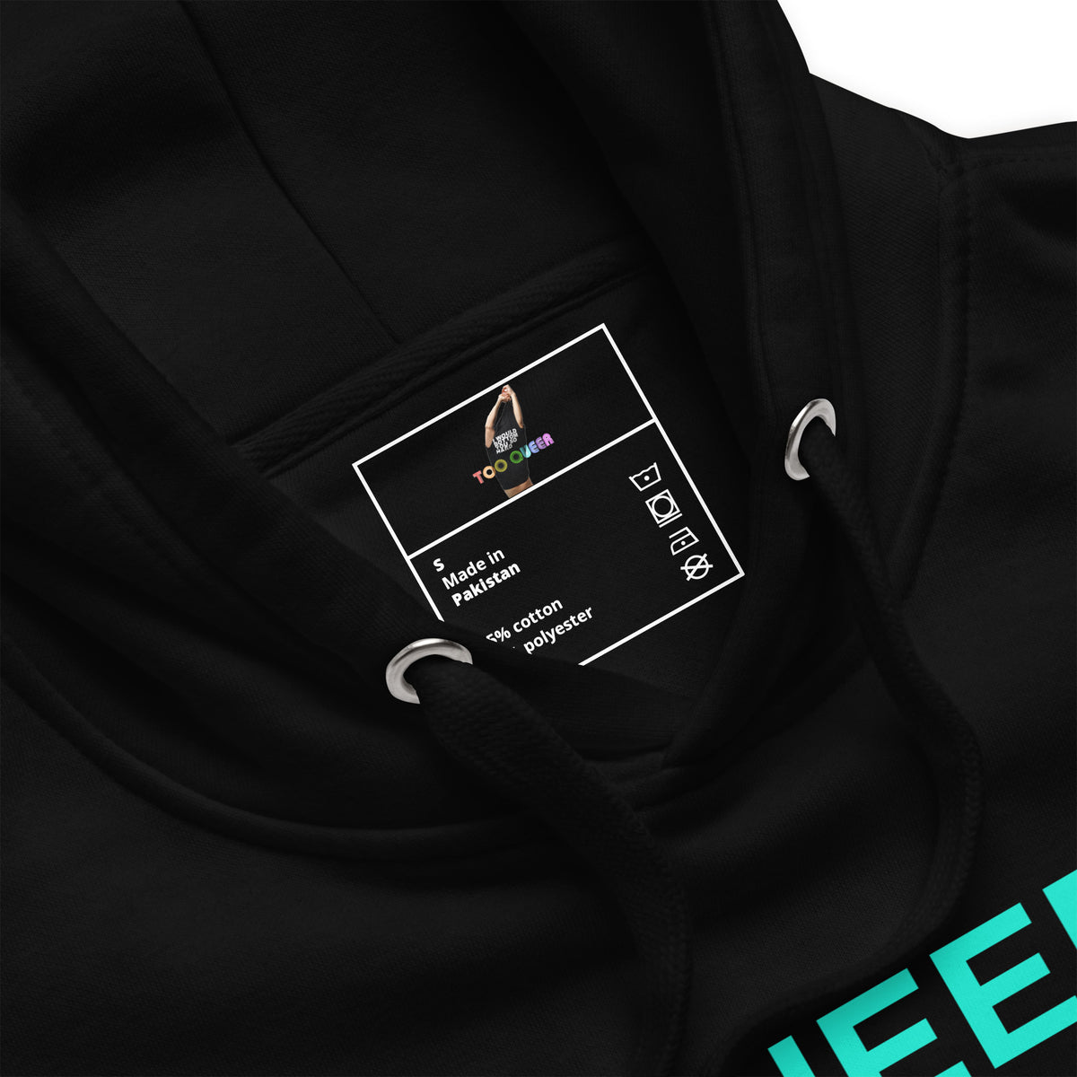 Close-up of a black hoodie showing the inner neck label with 'TooLoud' branding and 'Made in Pakistan' text, along with metal drawstring rings and a partial teal graphic on the sleeve.
