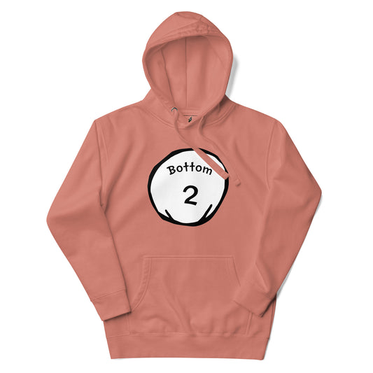 A dusty rose pink pullover hoodie with a graphic print on the chest. The graphic is a white circle with black outlines containing the text 'Bottom 2' and a small orange slice detail.