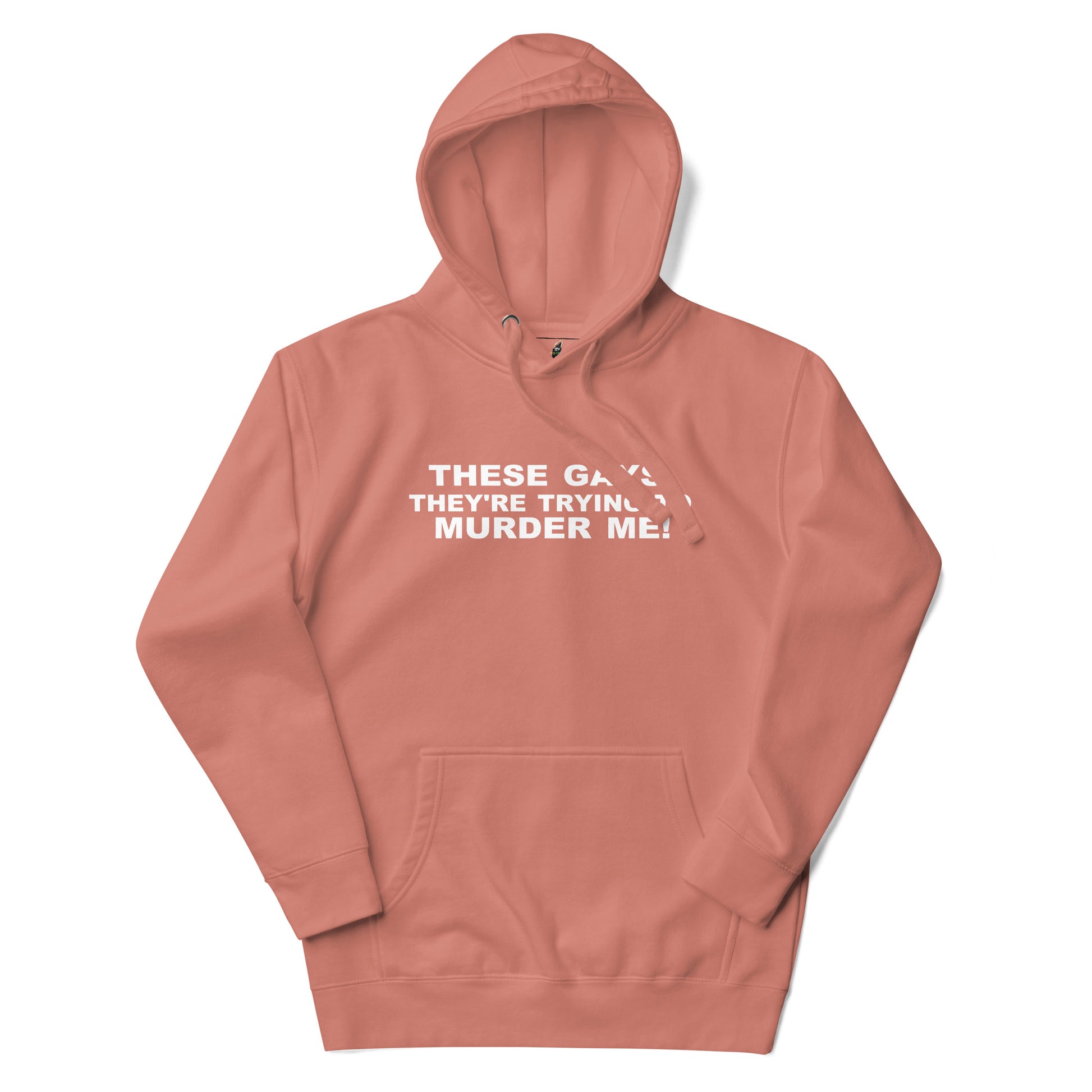 A dusty rose pink pullover hoodie with white text on the chest reading 'THESE GAYS THEY'RE TRYING TO MURDER ME!', displayed on a clean white background.