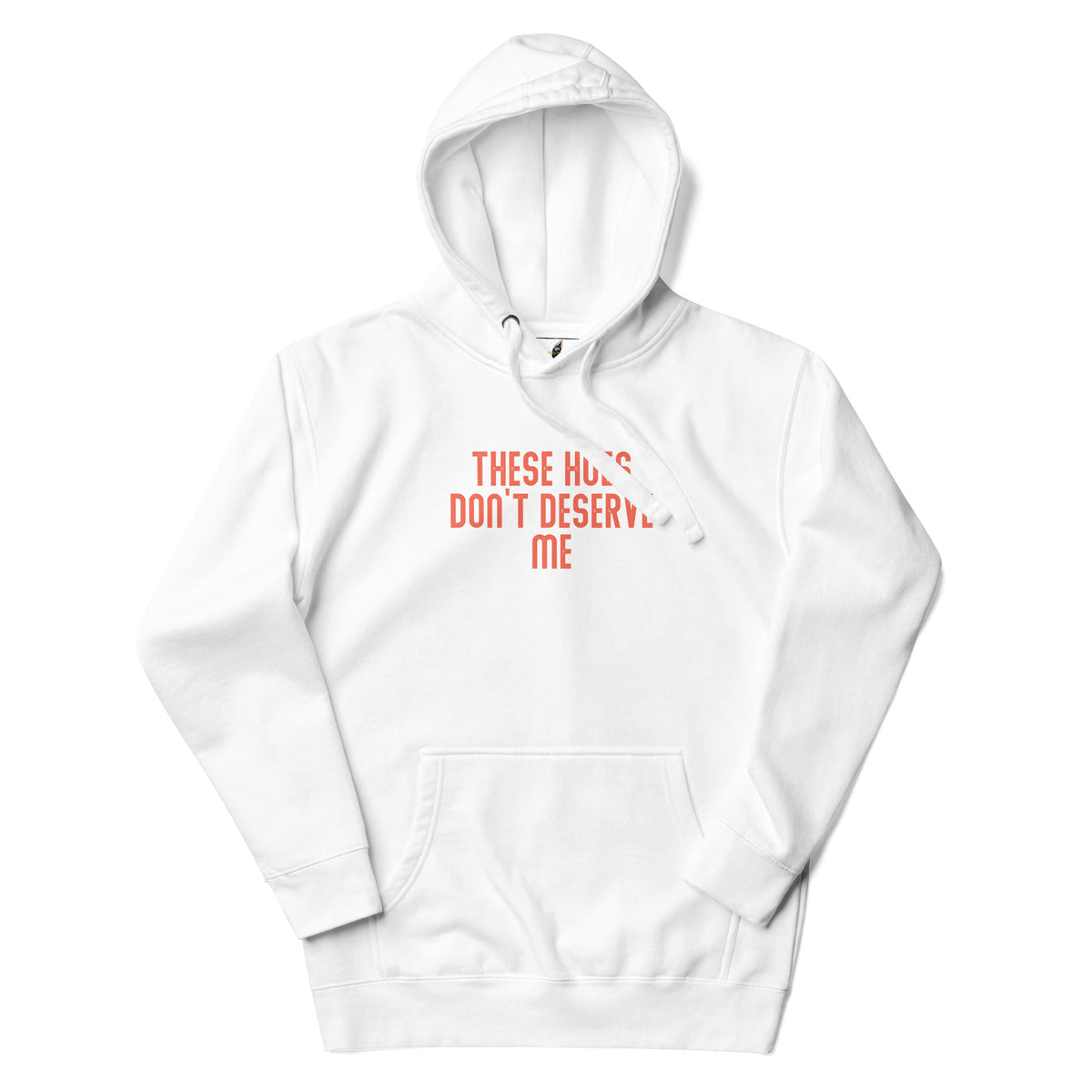 A white pullover hoodie with a kangaroo pocket and a chest graphic that reads 'THESE HUGS DON'T DESERVE ME' in a coral pink color, shown against a plain white background.