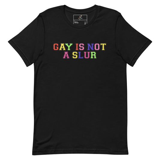 A black short-sleeve crewneck t-shirt featuring the text 'GAY IS NOT A SLUR' printed across the chest in a vibrant rainbow gradient font.