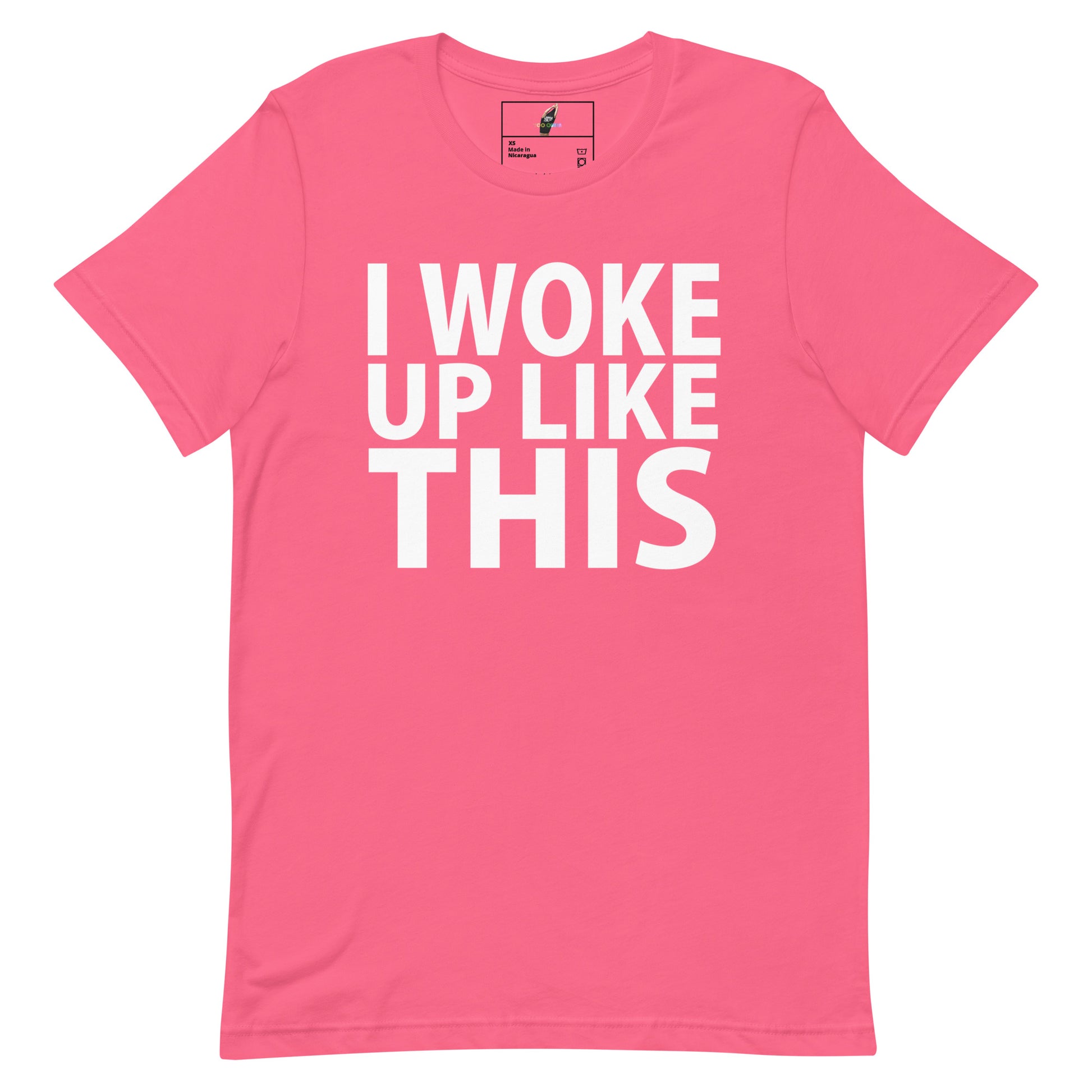 A pink short-sleeve crewneck t-shirt with bold white text on the front reading 'I WOKE UP LIKE THIS'. The shirt is displayed flat against a solid white background, with a small brand label visible inside the collar.