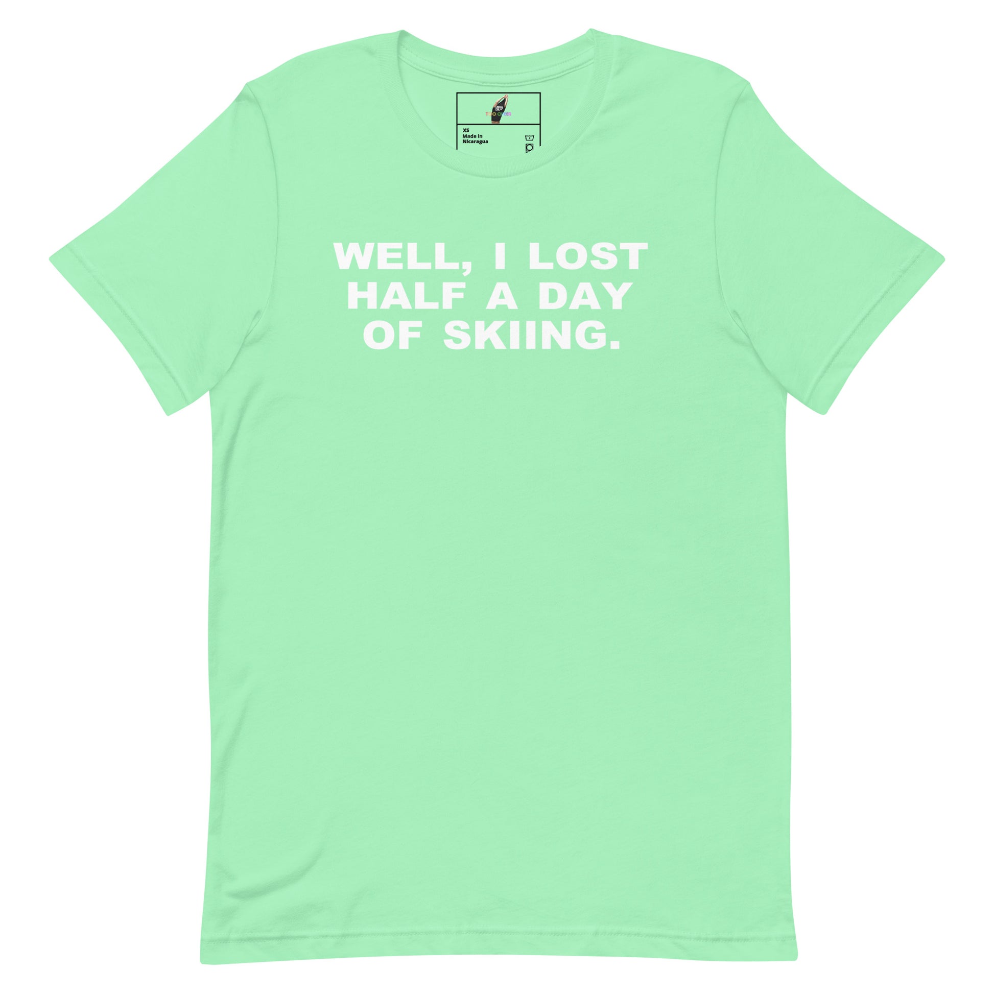 A mint green short-sleeve t-shirt with the phrase 'WELL, I LOST HALF A DAY OF SKIING.' printed in white block letters across the chest, displayed flat against a white background.