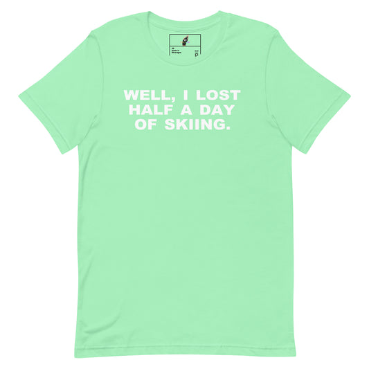 A mint green short-sleeve t-shirt with the phrase 'WELL, I LOST HALF A DAY OF SKIING.' printed in white block letters across the chest, displayed flat against a white background.