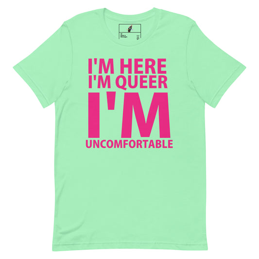 A mint green short-sleeve t-shirt with bold hot pink text on the front reading 'I'M HERE I'M QUEER I'M UNCOMFORTABLE'.