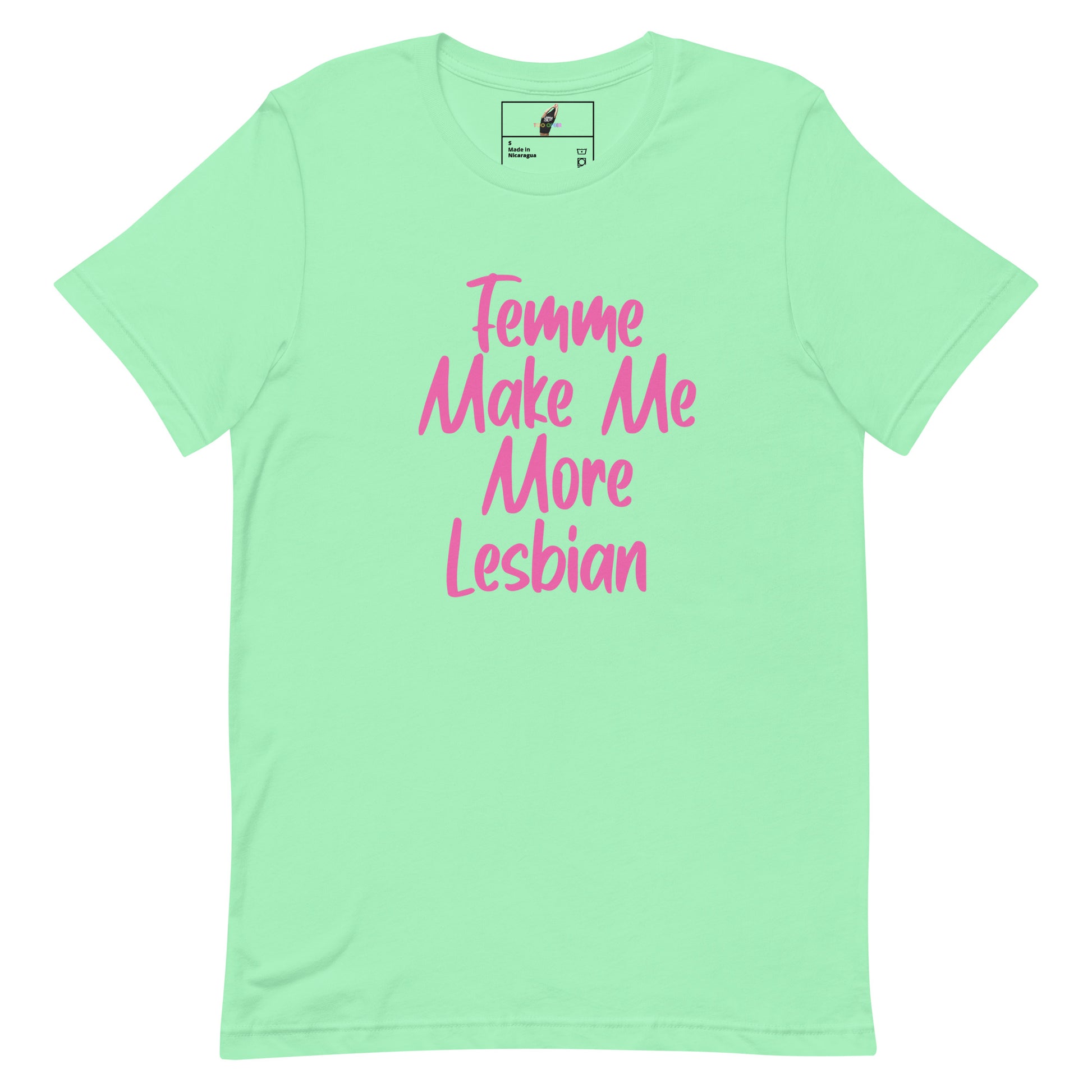 A mint green short-sleeve t-shirt with pink text on the front reading 'Femme Make Me More Lesbian'. The shirt is displayed flat against a solid white background, with a small brand label visible inside the collar.